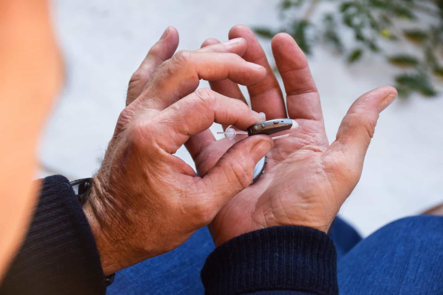 Two male hands hold two small, gray Lexie Lumen quality hearing aids after taking a fast online hearing test
