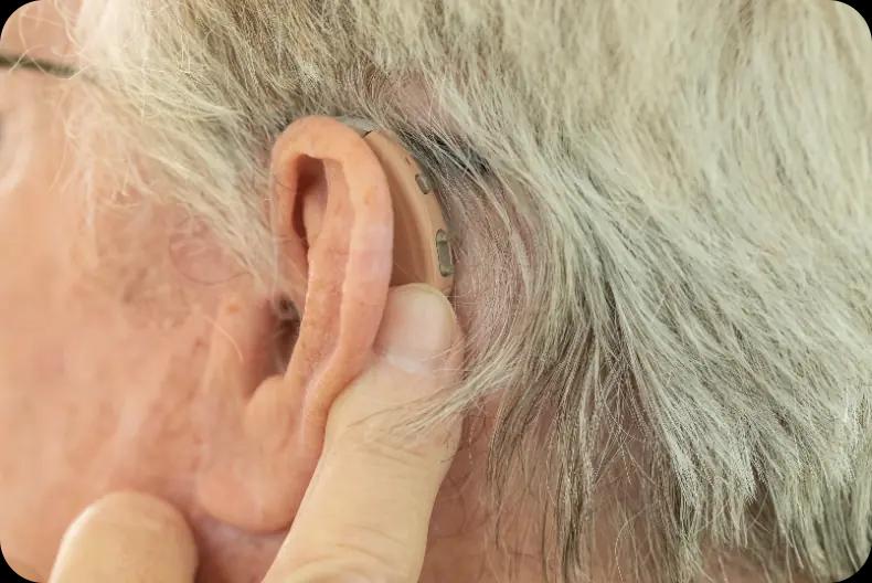 Hearing aid on ear of man with grey hair.