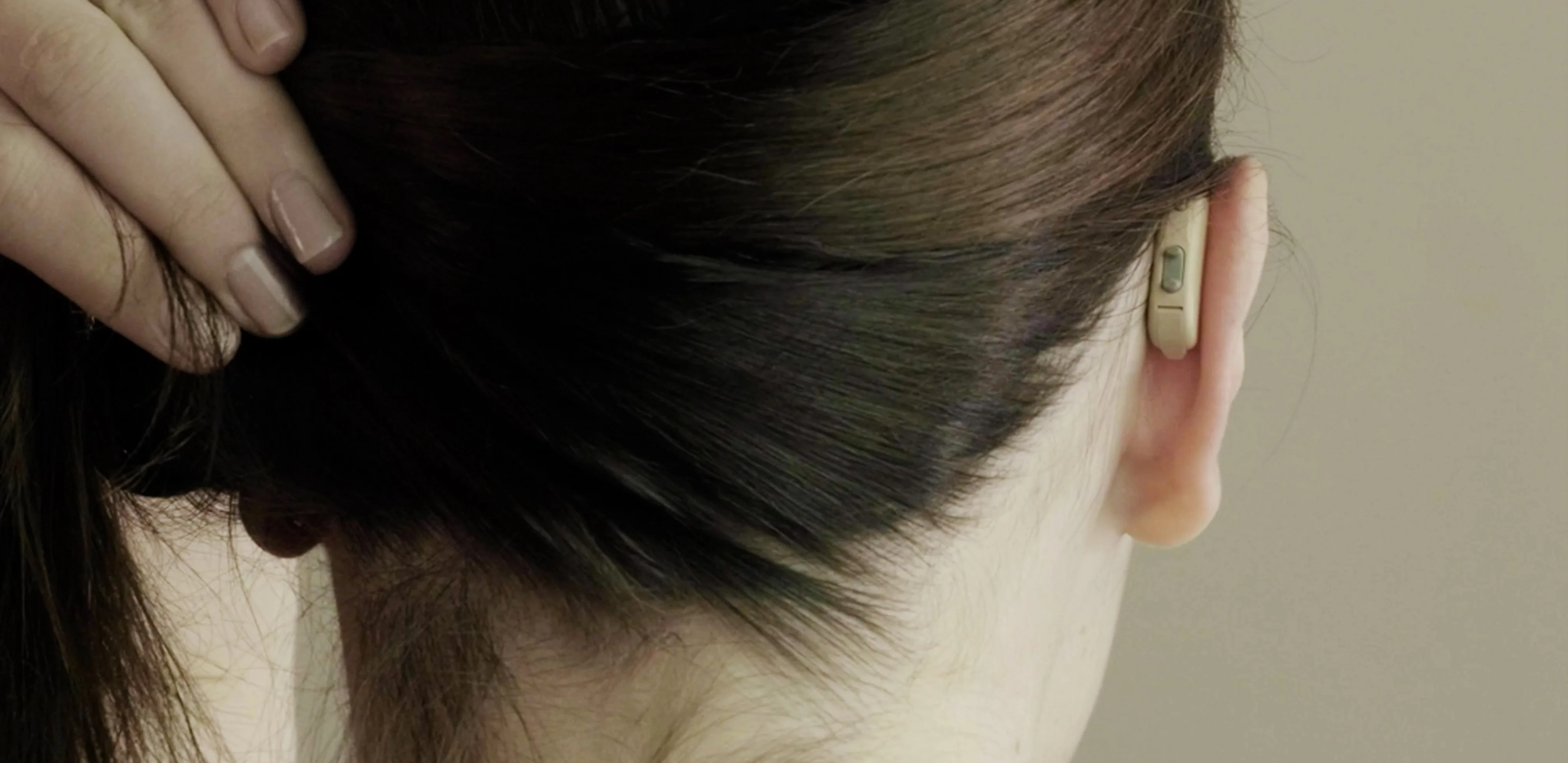 Behind shot of a dark-haired woman wearing a beige Lexie Lumen hearing aid.