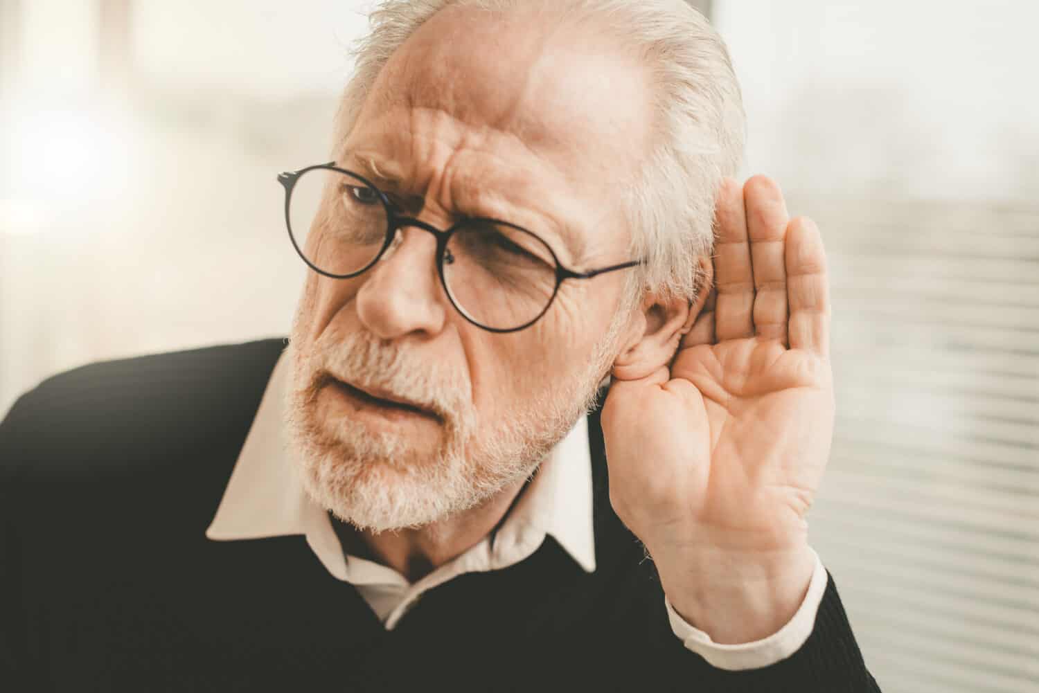 senior with age-related hearing loss cupping his ear
